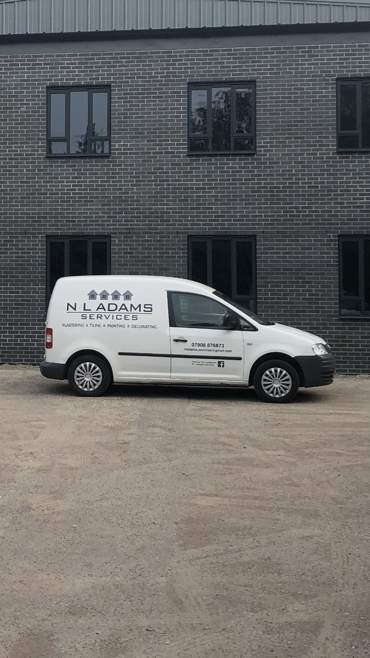 The white N L Adams Services van with its livery, parked outside a building